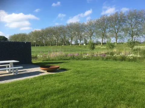 Gazon, terras met picknicktafel en vuurschaal naast de bloemenweide
