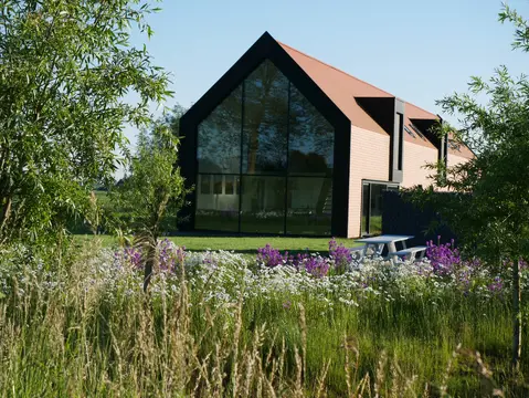 Glazen puntgevel van Trimaarzate achter de bloemenweide
